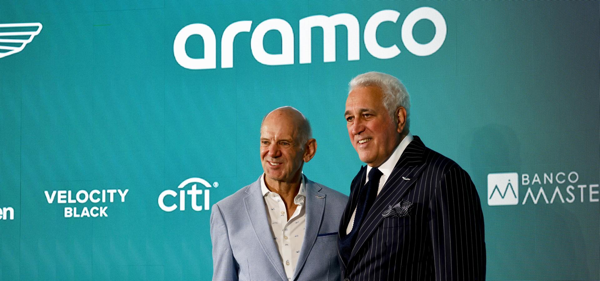 Two men wearing suits, smiling, in front of a green background