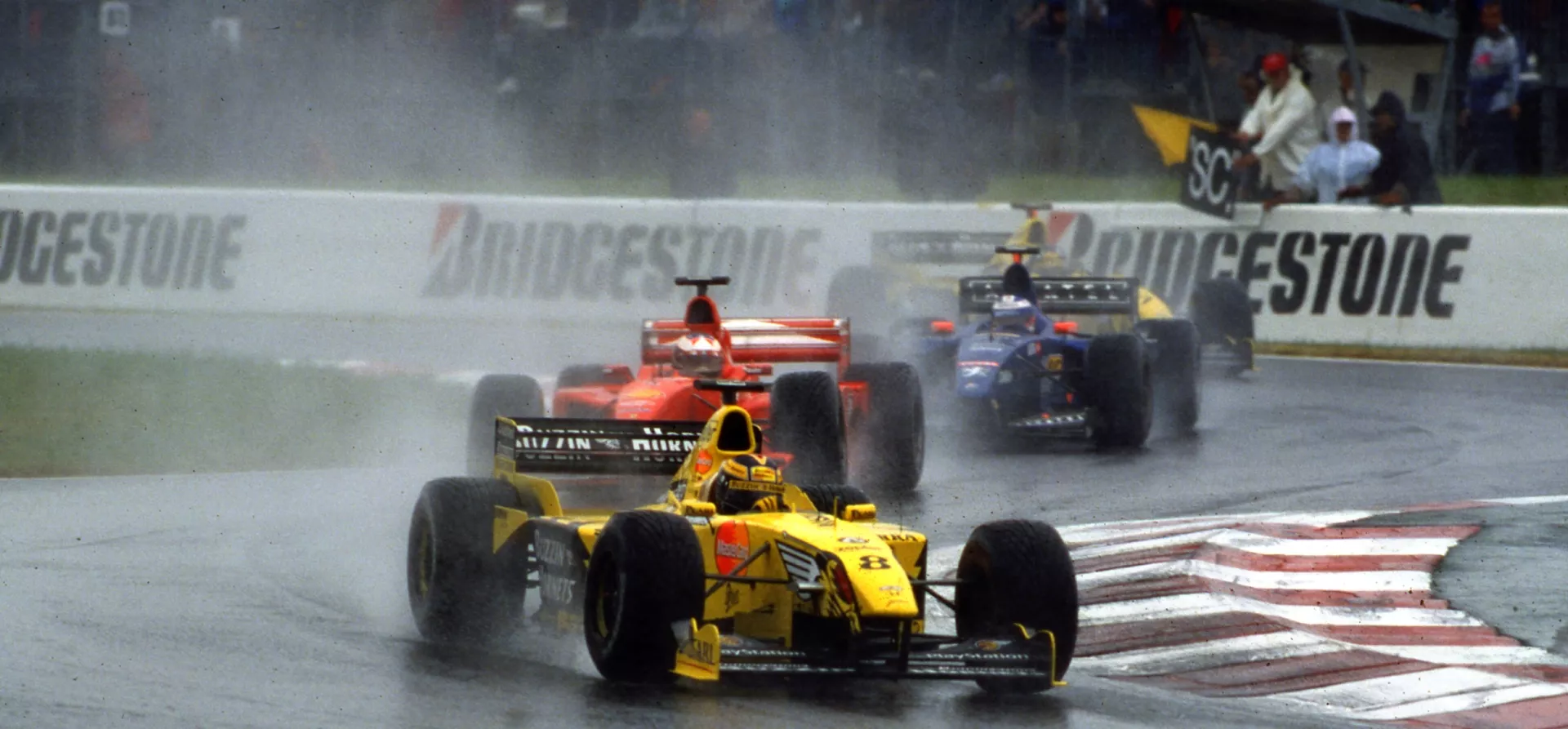 Yellow F1 car leading a red F1 car in the rain