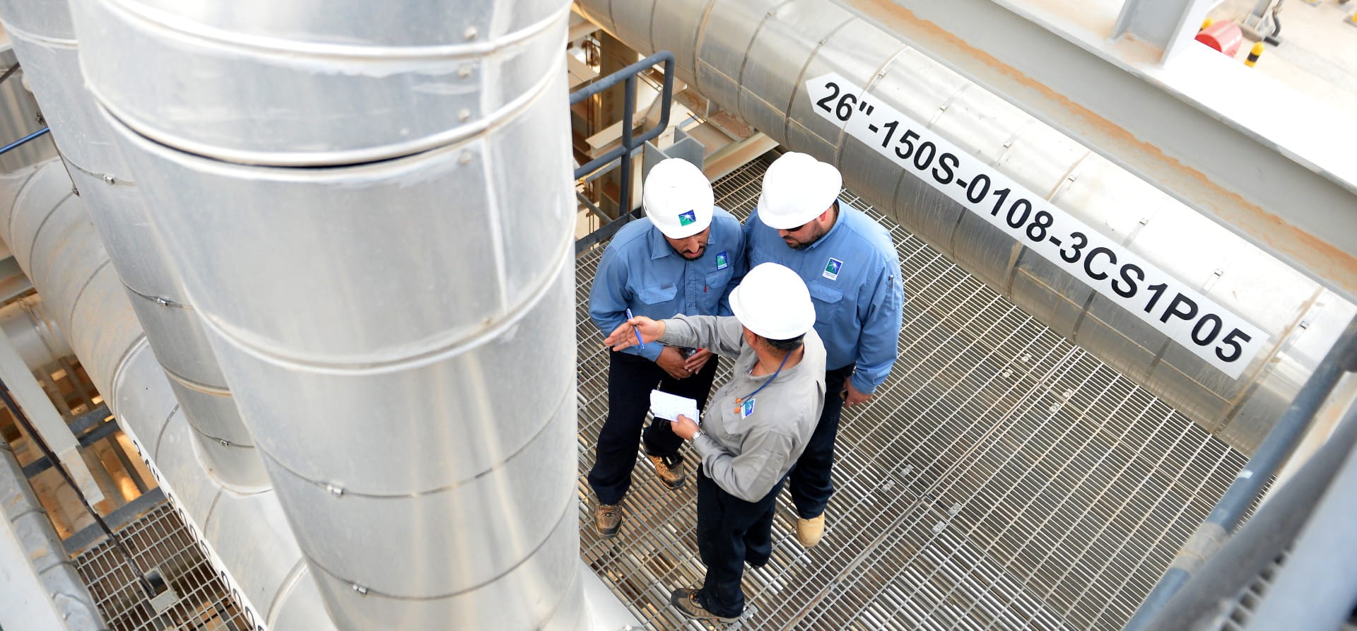 Oil plant operators wearing helmets and looking at a pipe