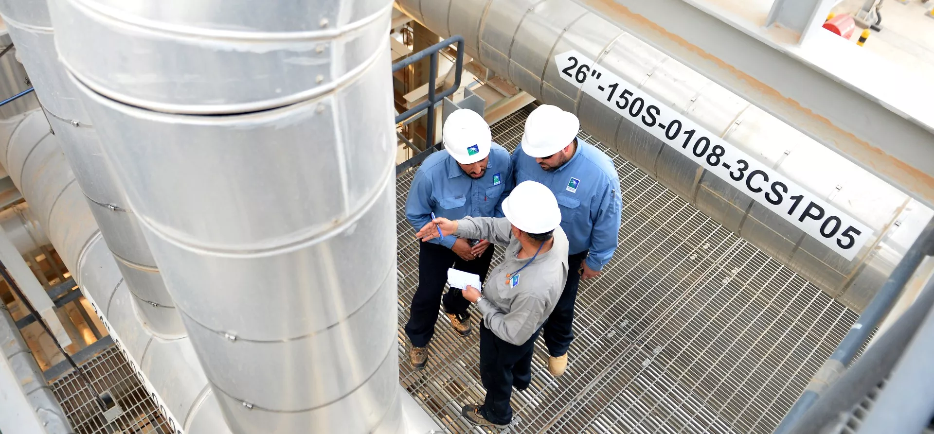 Oil plant operators wearing helmets and looking at a pipe