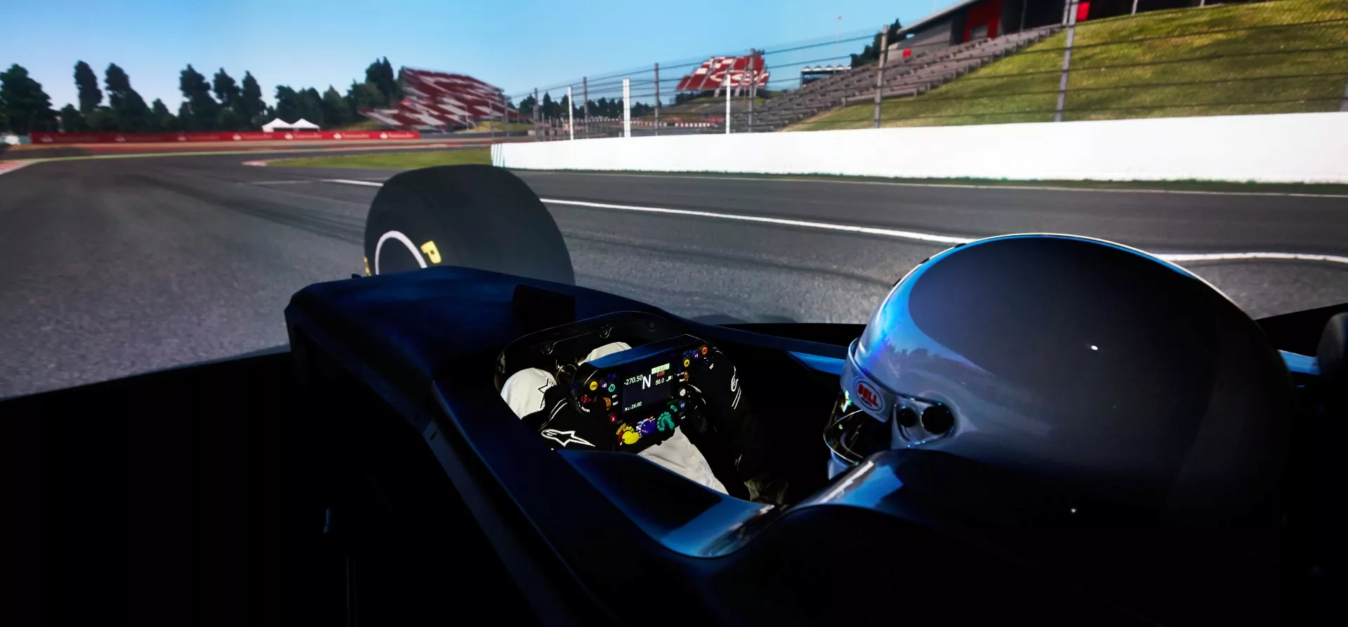 photo of an F1 simulator with a driver wearing a white helmet watching a screen and holding a steering wheel