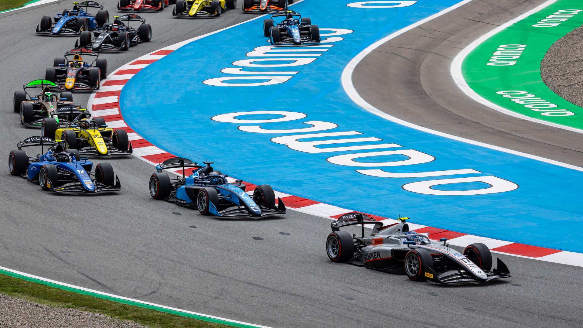Start of the 2024 Formula 2 Spanish Feature Race - a grey car leads a field of F2 cars around the first two winding corners of the circuit in Spain