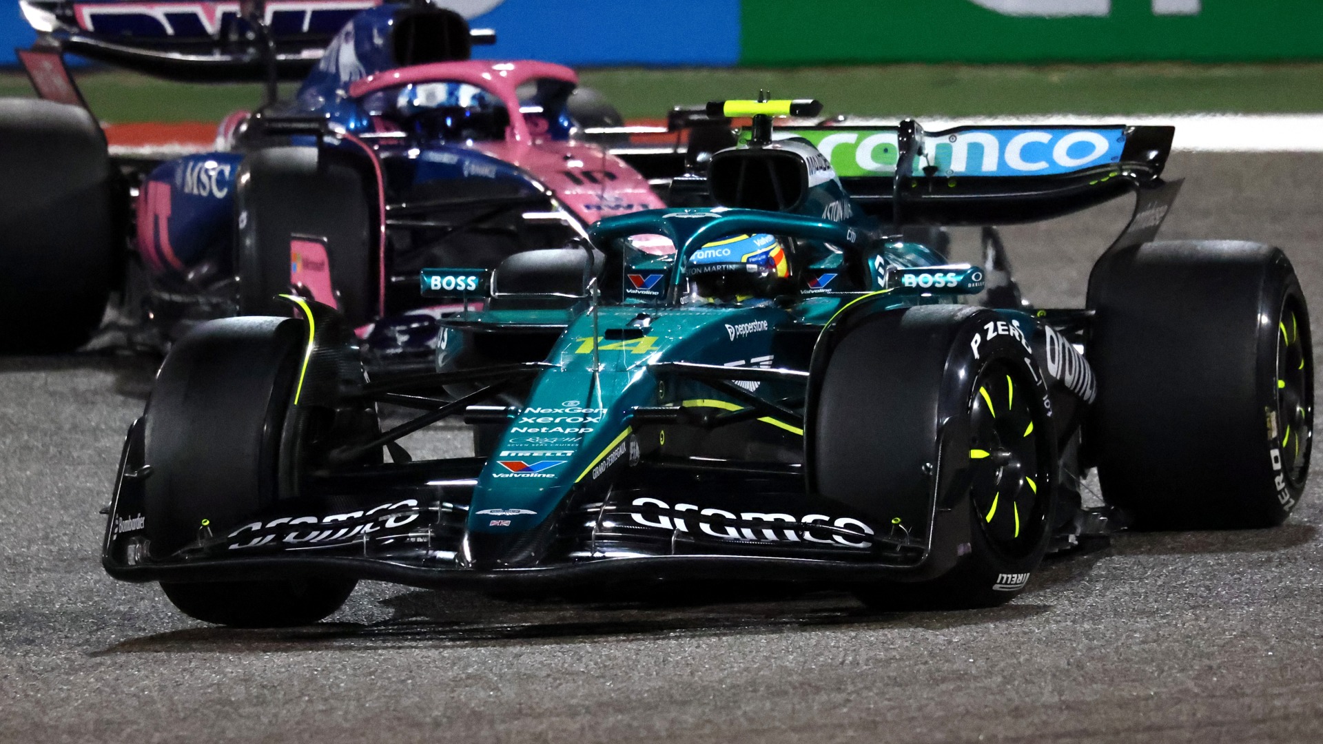 Aston Martin and Alpine F1 cars rounding a corner in the dark at 2025 pre-season testing in Bahrain