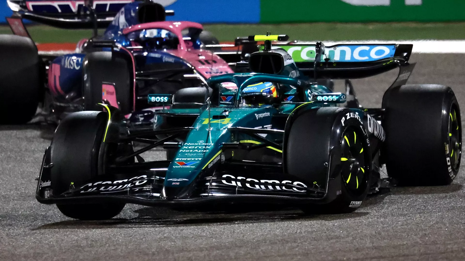 Aston Martin and Alpine F1 cars rounding a corner in the dark at 2025 pre-season testing in Bahrain